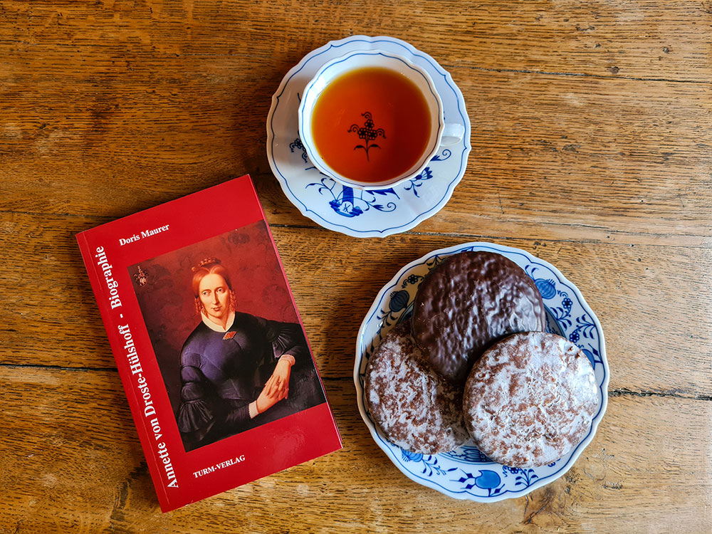 Buch "Annette von Droste-Hülshoff - Biographie" mit einer Tasse Tee und Kuchen.